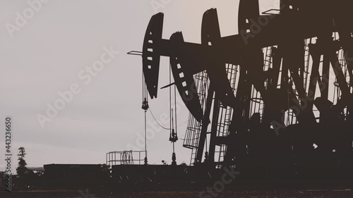 Silhouette of oil extracting operation by pump jack in the oil field
