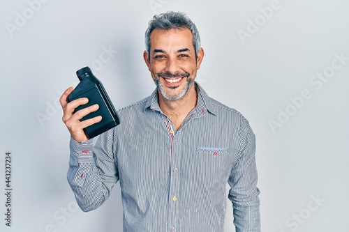 Handsome middle age man with grey hair holding motor oil bottle looking positive and happy standing and smiling with a confident smile showing teeth © Krakenimages.com