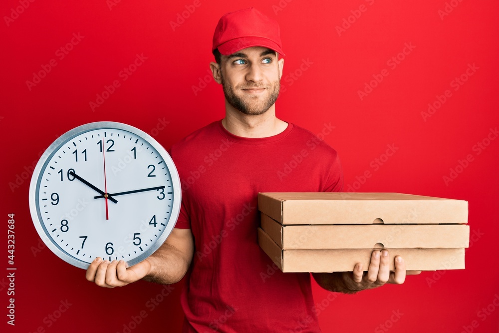 Young caucasian man holding delivery package and clock smiling looking to the side and staring away thinking. Young caucasian man holding delivery package and clock smiling looking to the side and staring away thinking.