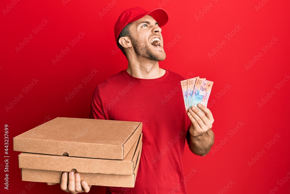 Young caucasian man holding delivery box and swiss franc banknotes angry and mad screaming frustrated and furious, shouting with anger looking up. Young caucasian man holding delivery box and swiss franc banknotes angry and mad screaming frustrated and furious, shouting with anger looking up.