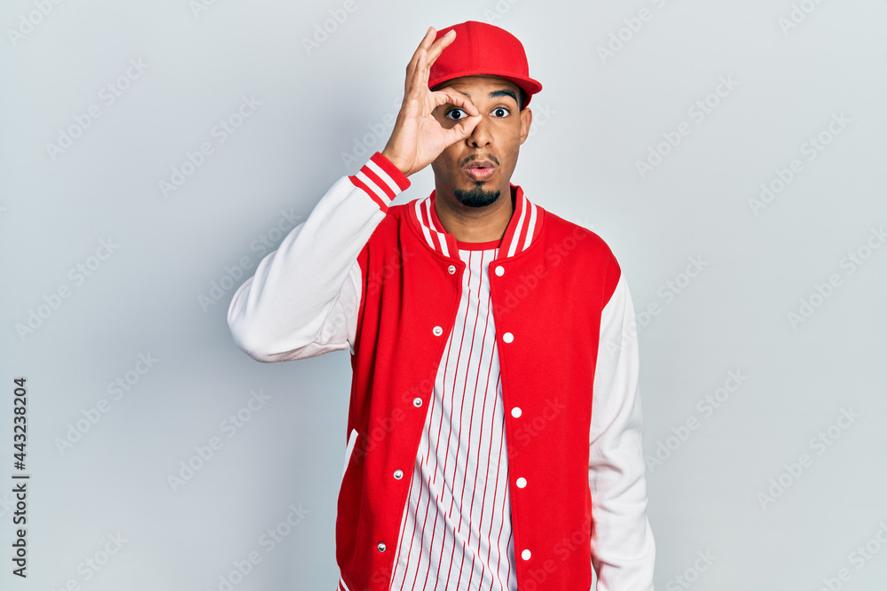 Young african american man wearing baseball uniform doing ok gesture shocked with surprised face, eye looking through fingers. unbelieving expression.