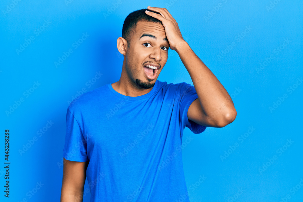Young african american man wearing casual blue t shirt surprised with hand on head for mistake, remember error. forgot, bad memory concept. Young african american man wearing casual blue t shirt surprised with hand on head for mistake, remember error. forgot, bad memory concept.