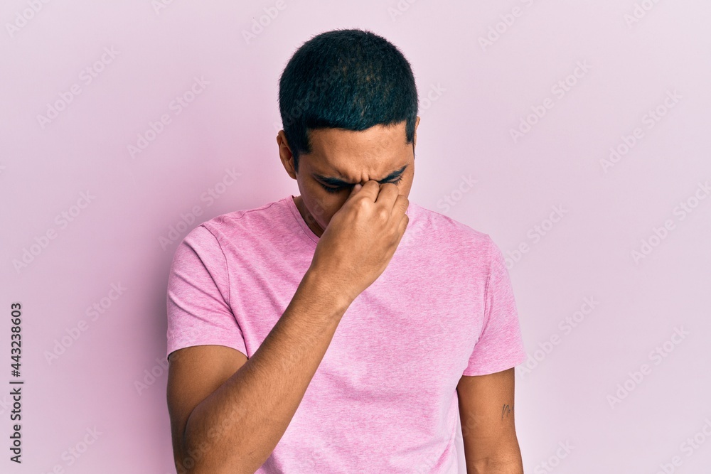 Young handsome hispanic man wearing casual pink t shirt tired rubbing nose and eyes feeling fatigue and headache. stress and frustration concept. Young handsome hispanic man wearing casual pink t shirt tired rubbing nose and eyes feeling fatigue and headache. stress and frustration concept.