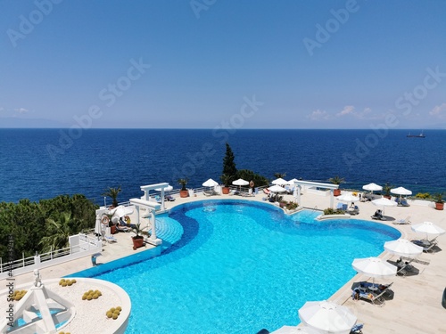 Luxurious pool with blue water and sea views. Sun loungers and umbrellas near the pool in the resort of Kusadasi, Turkey.