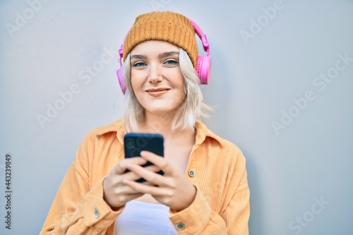 Young blonde girl smiling happy using smartphone and headphones at the city.