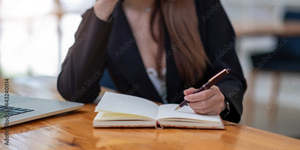 Close up woman's hands with laptop computer, notebook and pen taking notes in business office Close up woman's hands with laptop computer, notebook and pen taking notes in business office