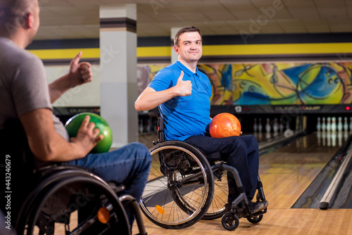 Two young disabled men in wheelchairs playing bowling in the club © romaset