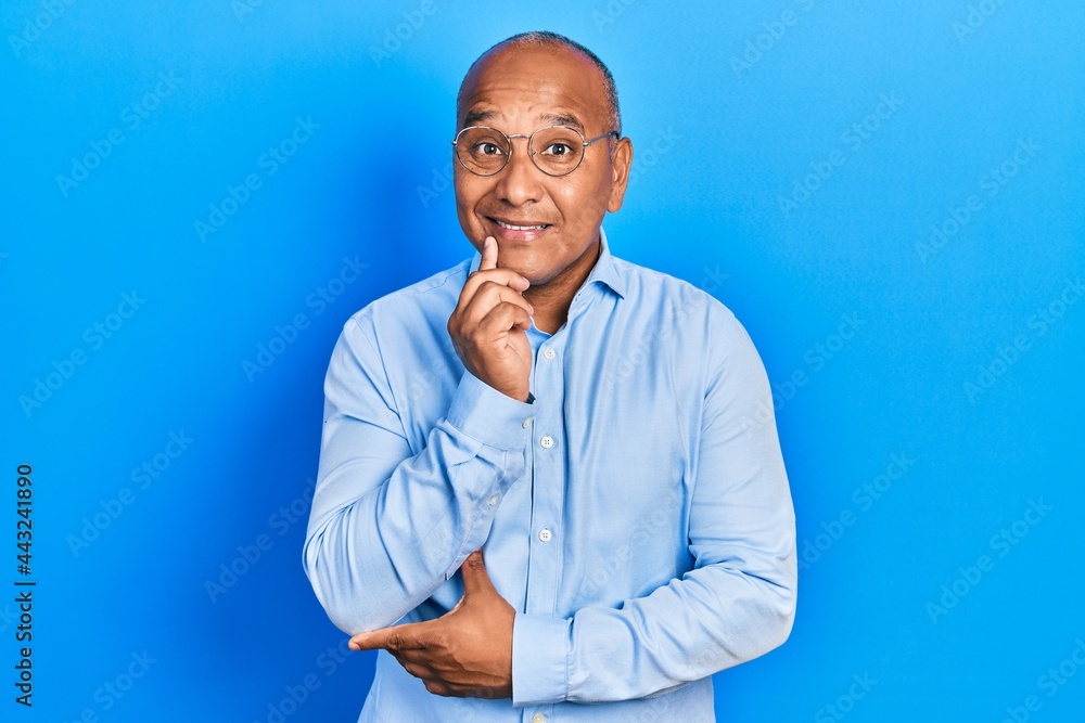 Middle age latin man wearing casual clothes and glasses looking confident at the camera with smile with crossed arms and hand raised on chin. thinking positive. Middle age latin man wearing casual clothes and glasses looking confident at the camera with smile with crossed arms and hand raised on chin. thinking positive.