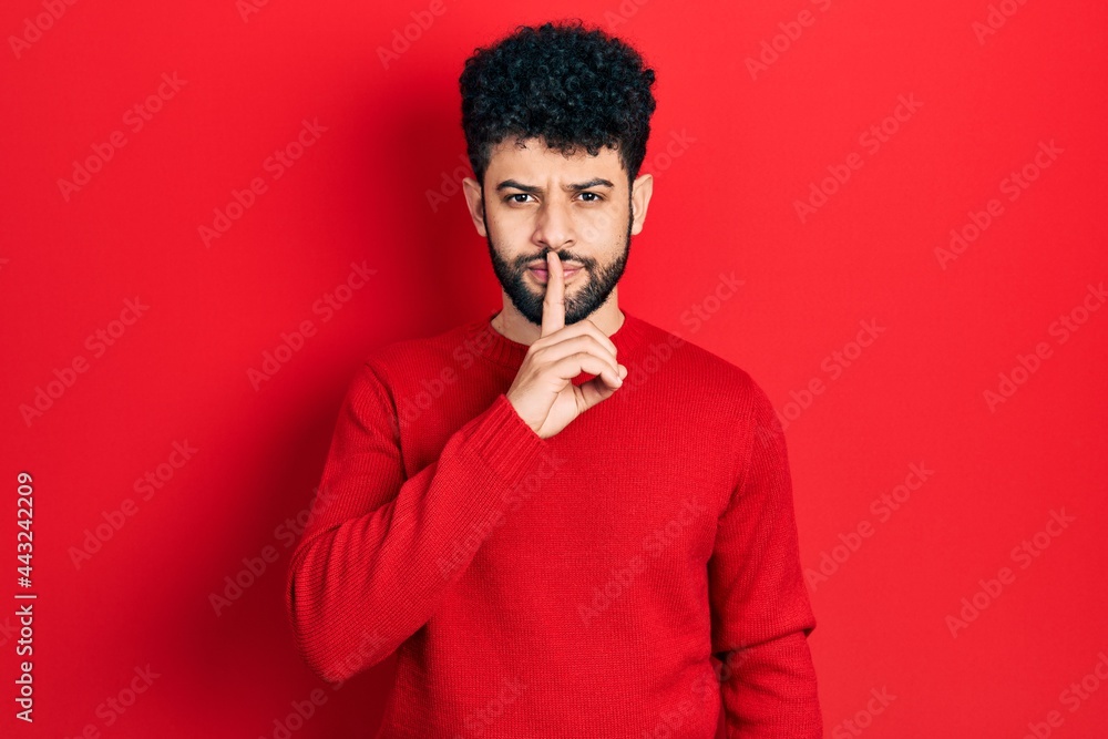Young arab man with beard wearing casual red sweater asking to be quiet with finger on lips. silence and secret concept.