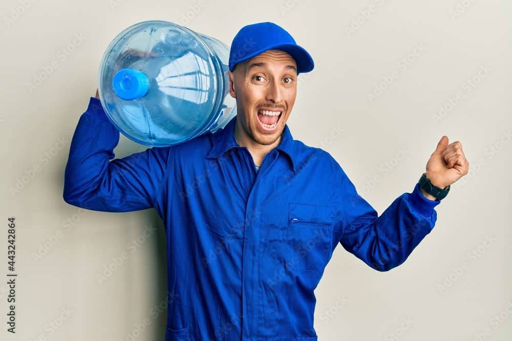 Bald courier man with beard holding a gallon bottle of water for delivery celebrating victory with happy smile and winner expression with raised hands