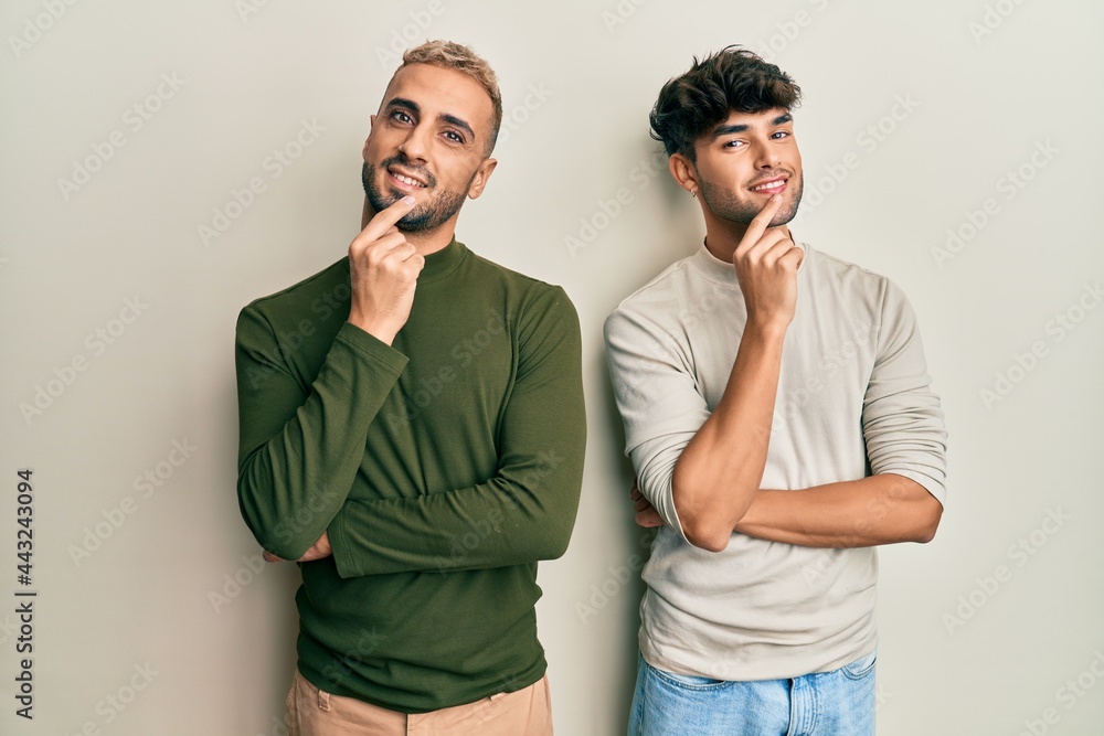 Homosexual gay couple standing together wearing casual clothes smiling looking confident at the camera with crossed arms and hand on chin. thinking positive. Homosexual gay couple standing together wearing casual clothes smiling looking confident at the camera with crossed arms and hand on chin. thinking positive.