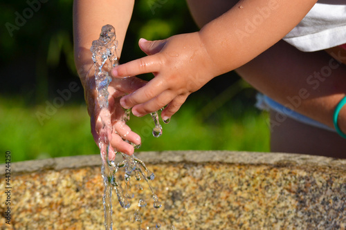 Primer plano de las manos de una niña acariciando, e intentando atrapar, el agua que mana de una fuente en un parque