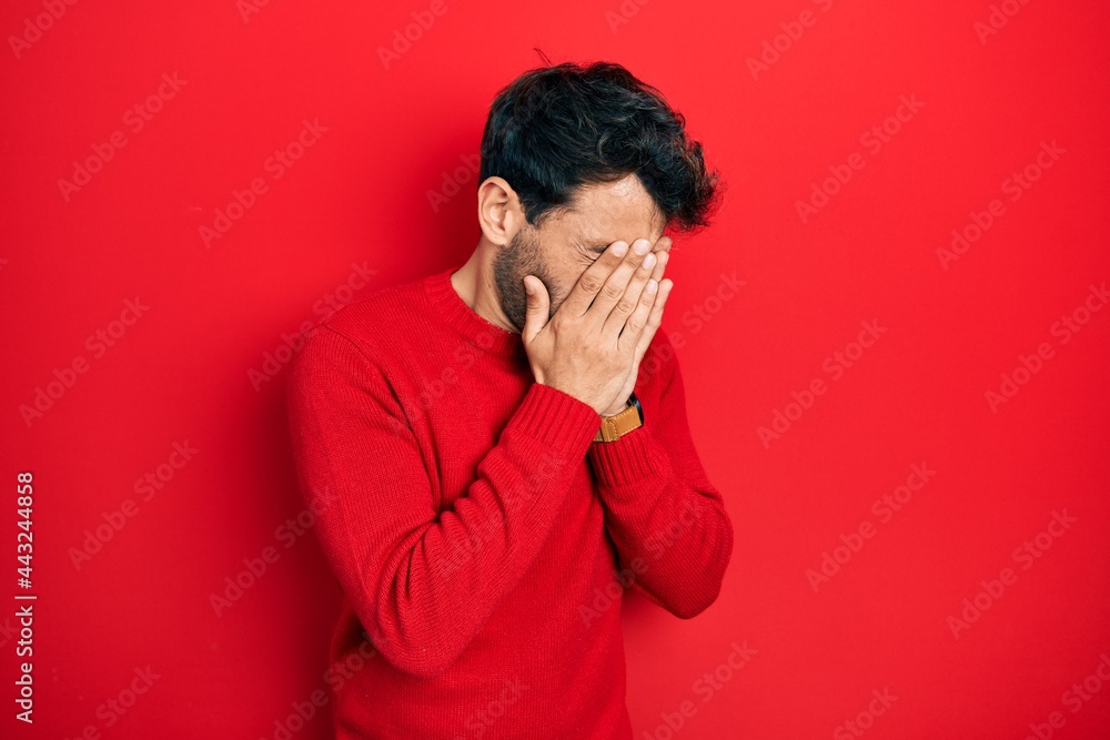 Handsome man with beard wearing casual red sweater with sad expression covering face with hands while crying. depression concept. Handsome man with beard wearing casual red sweater with sad expression covering face with hands while crying. depression concept.