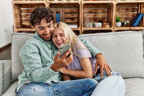 Young couple using smartphone sitting on the sofa at home. © Krakenimages.com