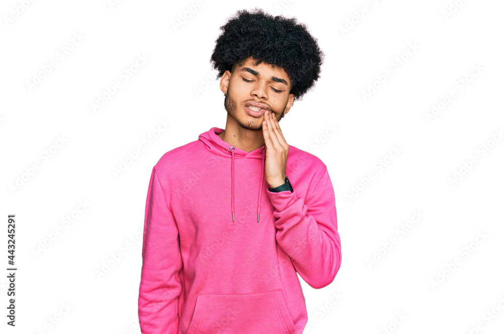 Young african american man with afro hair wearing casual pink sweatshirt touching mouth with hand with painful expression because of toothache or dental illness on teeth. dentist Young african american man with afro hair wearing casual pink sweatshirt touching mouth with hand with painful expression because of toothache or dental illness on teeth. dentist