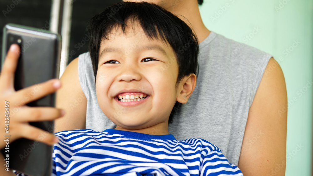 Asian child boy smiling with happy face, hand holding smartphone, in hug of father. Dad and child have happy moment together. Concept of good relationship, technology connection, father's day. Asian child boy smiling with happy face, hand holding smartphone, in hug of father. Dad and child have happy moment together. Concept of good relationship, technology connection, father's day.