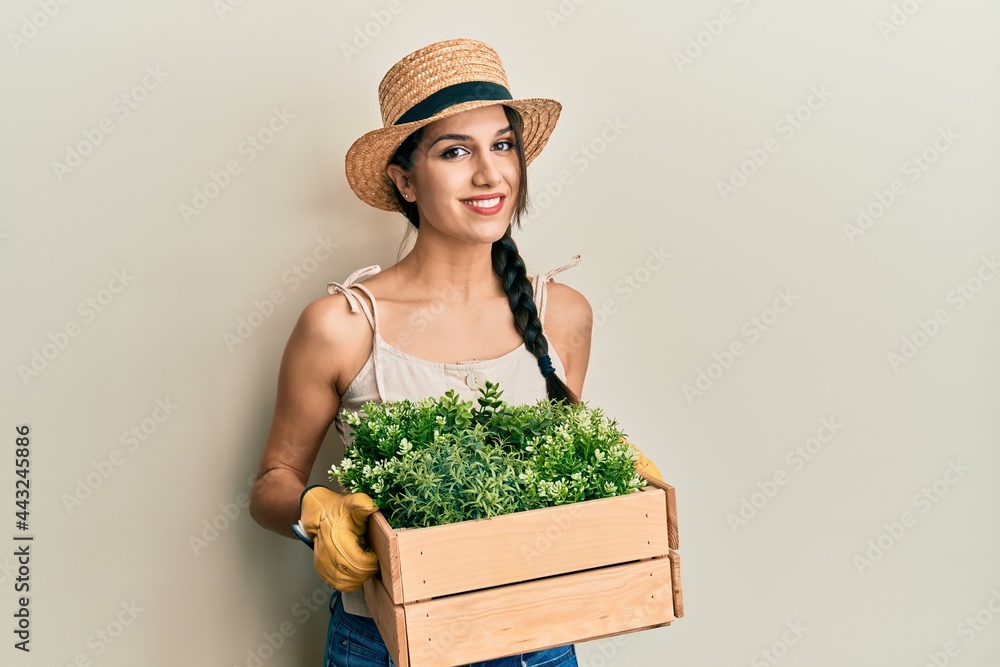 Young hispanic woman holding green plant pot relaxed with serious expression on face. simple and natural looking at the camera.