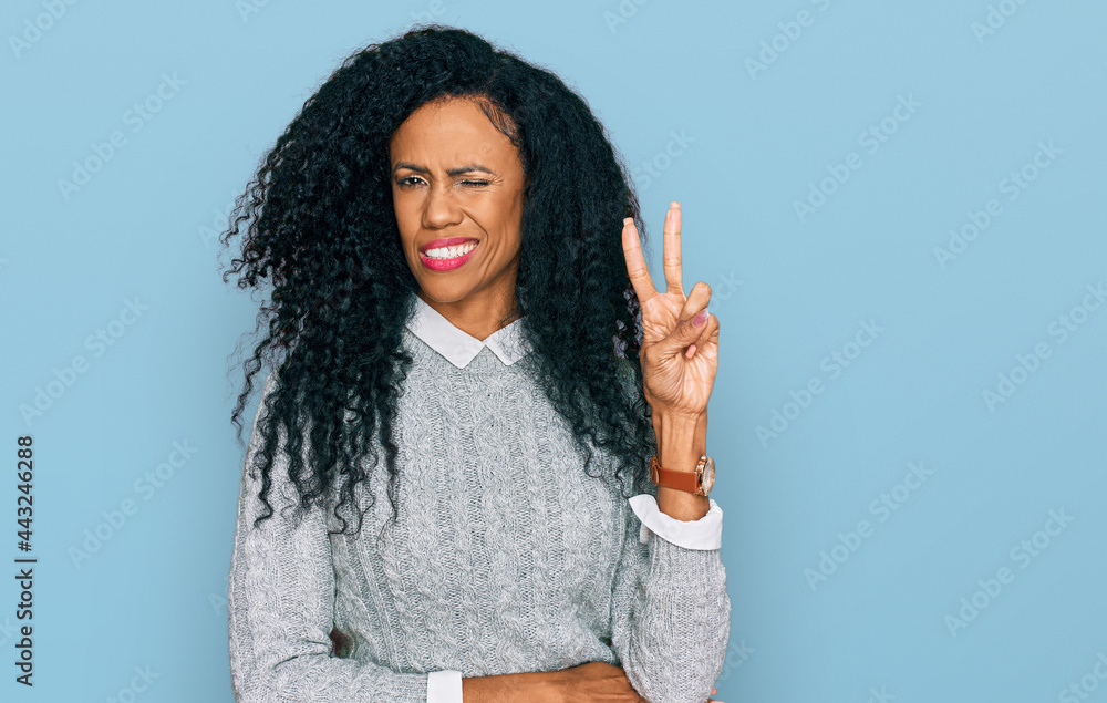 Middle age african american woman wearing casual clothes smiling with happy face winking at the camera doing victory sign with fingers. number two. Middle age african american woman wearing casual clothes smiling with happy face winking at the camera doing victory sign with fingers. number two.