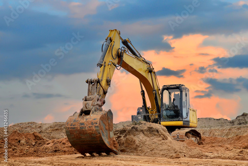 Excavator working on earthmoving at open pit mining on sunset background. Backhoe digs sand and gravel in quarry. Heavy construction equipment during excavation at construction site photo