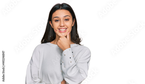 Young hispanic girl wearing casual clothes looking confident at the camera smiling with crossed arms and hand raised on chin. thinking positive.