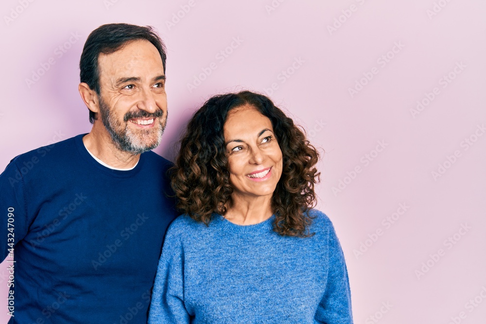 Middle age couple of hispanic woman and man hugging and standing together smiling looking to the side and staring away thinking. Middle age couple of hispanic woman and man hugging and standing together smiling looking to the side and staring away thinking.