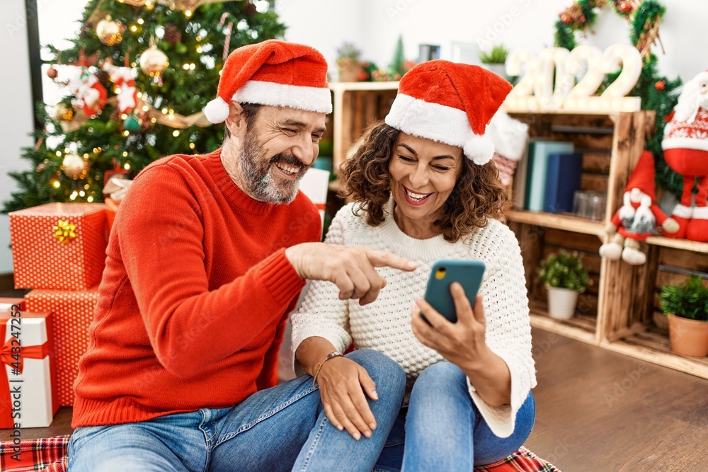 Middle age hispanic couple smiling happy wearing christmas hat. Sitting on the floor using smartphone at home. Middle age hispanic couple smiling happy wearing christmas hat. Sitting on the floor using smartphone at home.