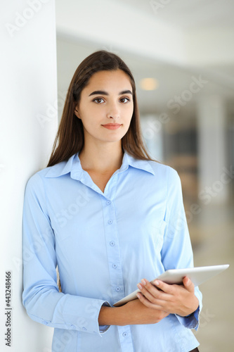 A friendly young businesswoman or female student is standing with some papers in the office. Lifestyle and diverse people concept