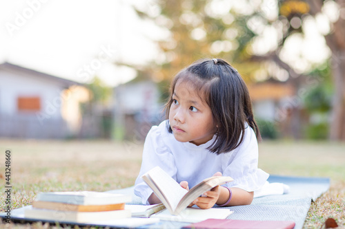 Kid lying down on yoga may enjoy reading her favorite book outdoors, Education concept of girl reading book © AlivePhoto