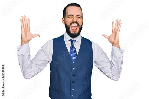 Young man with beard wearing business vest celebrating mad and crazy for success with arms raised and closed eyes screaming excited. winner concept