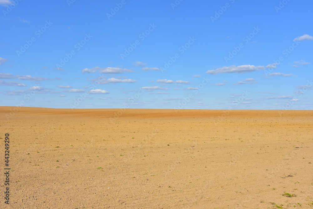 View of a deserted sand field against a blue sky with clouds.