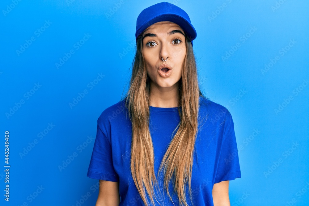 Young hispanic woman wearing delivery uniform and cap scared and amazed with open mouth for surprise, disbelief face Young hispanic woman wearing delivery uniform and cap scared and amazed with open mouth for surprise, disbelief face