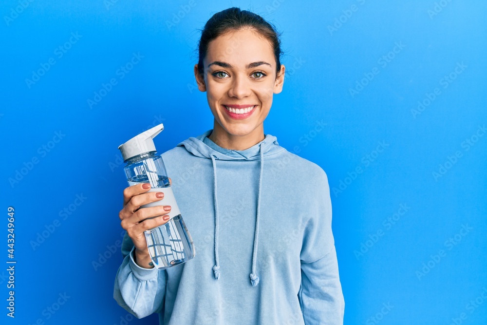 Young caucasian blonde woman drinking bottle of water looking positive and happy standing and smiling with a confident smile showing teeth Young caucasian blonde woman drinking bottle of water looking positive and happy standing and smiling with a confident smile showing teeth