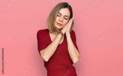 Young blonde girl wearing casual clothes sleeping tired dreaming and posing with hands together while smiling with closed eyes. © Krakenimages.com