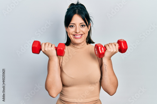 Young hispanic woman wearing sportswear using dumbbells smiling with a happy and cool smile on face. showing teeth.