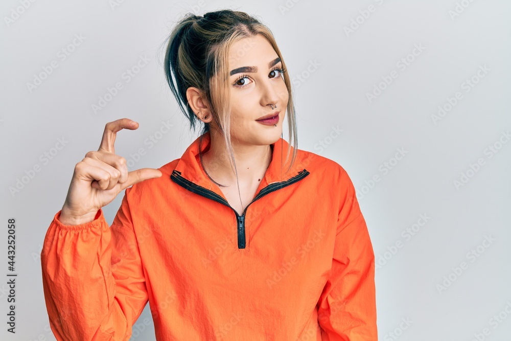 Young modern girl wearing sports sweatshirt smiling and confident gesturing with hand doing small size sign with fingers looking and the camera. measure concept. Young modern girl wearing sports sweatshirt smiling and confident gesturing with hand doing small size sign with fingers looking and the camera. measure concept.