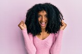 African american woman with afro hair wearing casual pink shirt celebrating surprised and amazed for success with arms raised and open eyes. winner concept.