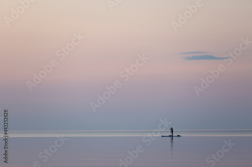 Man paddling on sup board on calm water in sunset. Supsurfing, water sport for active outdoor weekend. Silhouette view. Serenity