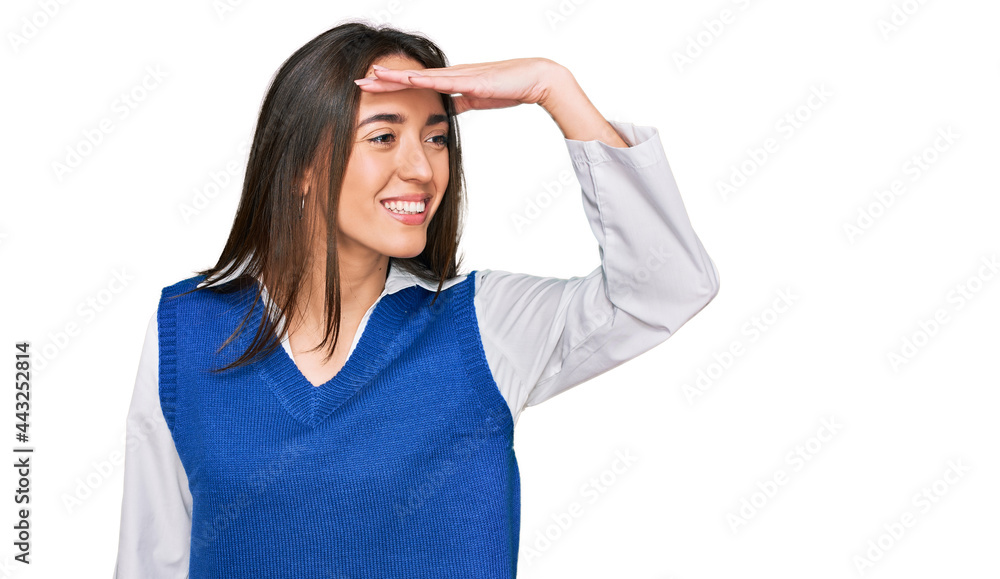 Young hispanic girl wearing casual clothes very happy and smiling looking far away with hand over head. searching concept. Young hispanic girl wearing casual clothes very happy and smiling looking far away with hand over head. searching concept.