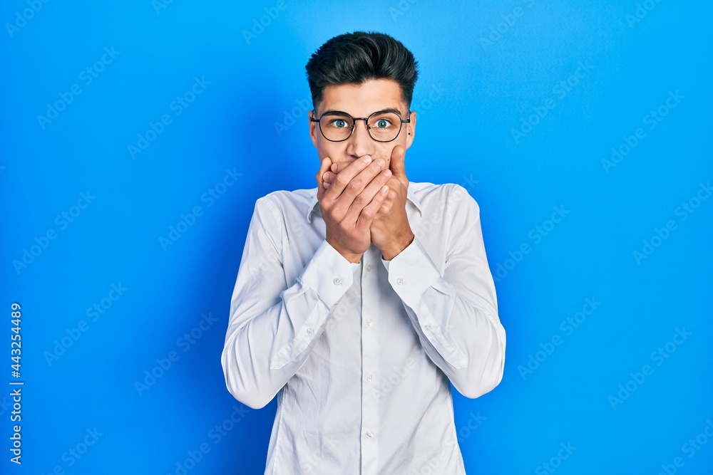 Young hispanic man wearing casual clothes and glasses shocked covering mouth with hands for mistake. secret concept.