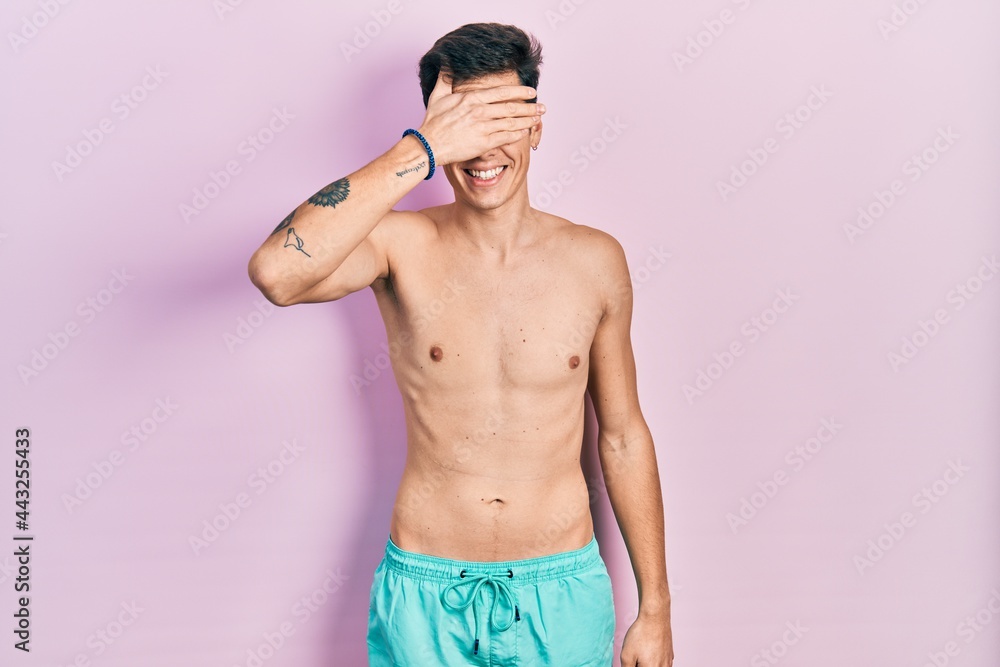 Fototapeta premium Young hispanic man wearing swimwear shirtless smiling and laughing with hand on face covering eyes for surprise. blind concept.