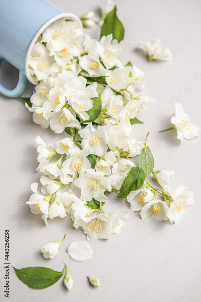 Fototapeta premium Floral composition on gray background with green leaves, flowers in cup flat lay