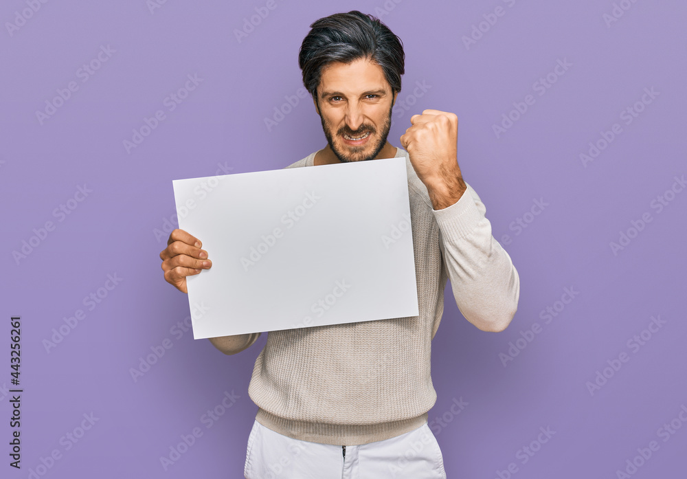 Young hispanic man holding blank empty banner annoyed and frustrated shouting with anger, yelling crazy with anger and hand raised Young hispanic man holding blank empty banner annoyed and frustrated shouting with anger, yelling crazy with anger and hand raised
