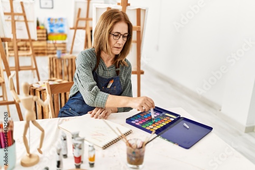 Middle age artist woman concentrated painting sitting on the table at art studio.