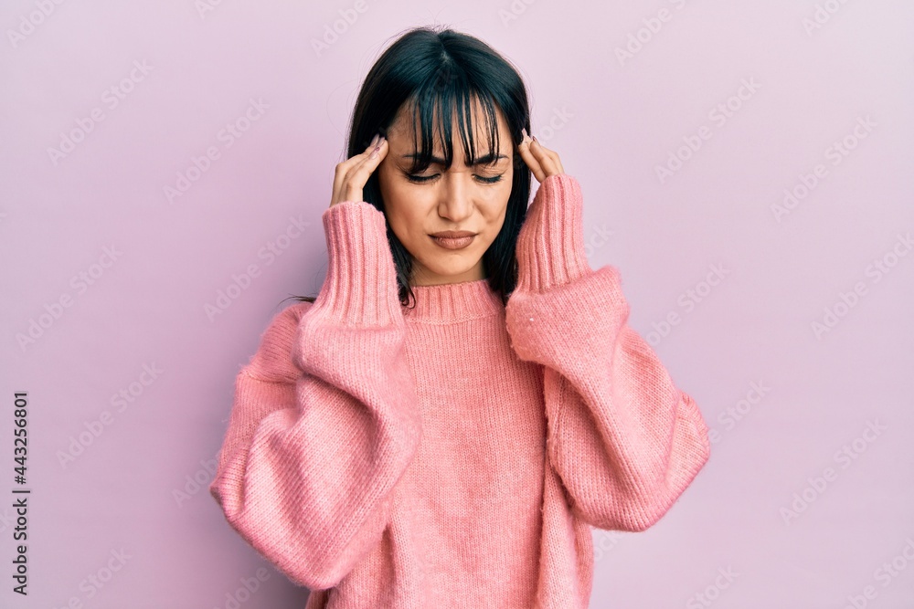 Young brunette woman with bangs wearing casual winter sweater with hand on head for pain in head because stress. suffering migraine. Young brunette woman with bangs wearing casual winter sweater with hand on head for pain in head because stress. suffering migraine.