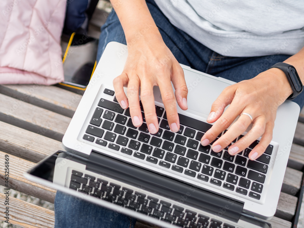 Woman sits with laptop on urban park bench. Freelancer at work. Student learns remotely from outdoors. Modern lifestyle. Woman sits with laptop on urban park bench. Freelancer at work. Student learns remotely from outdoors. Modern lifestyle.
