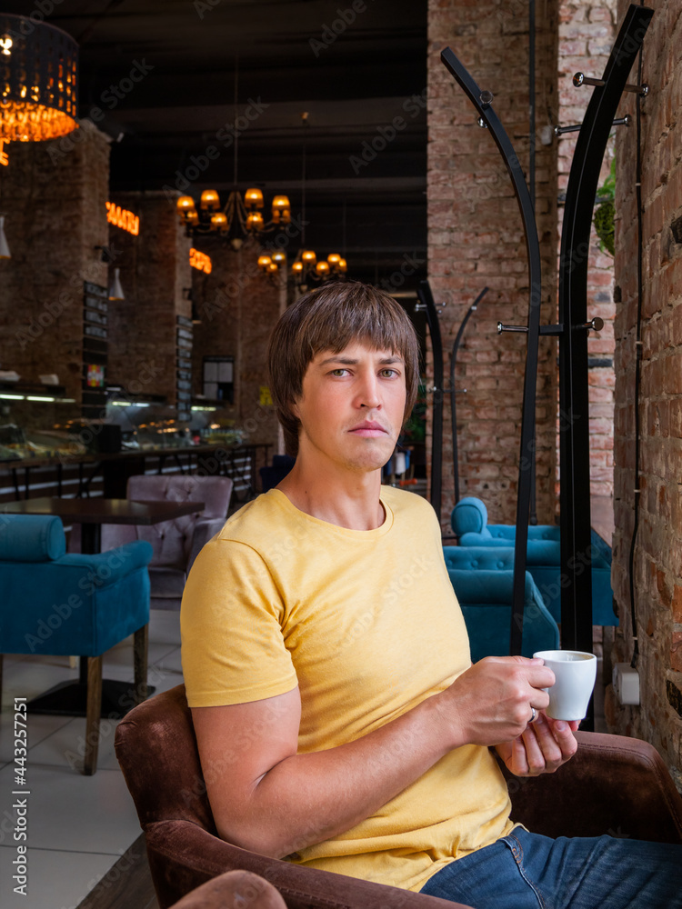 Fototapeta premium Man drinks coffee in cafe. Loft designed interior with red brick walls and plush chairs. Breakfast and morning cup of coffee away from home.