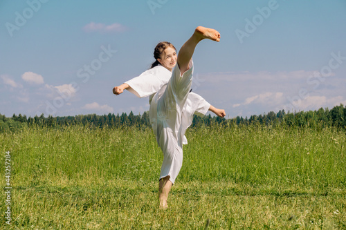 teen girl training karate kata outdoors, performs roundhouse kick ushiro mawashi geri photo