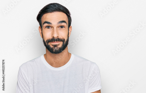 Young hispanic man wearing casual white t shirt puffing cheeks with funny face. mouth inflated with air, crazy expression.