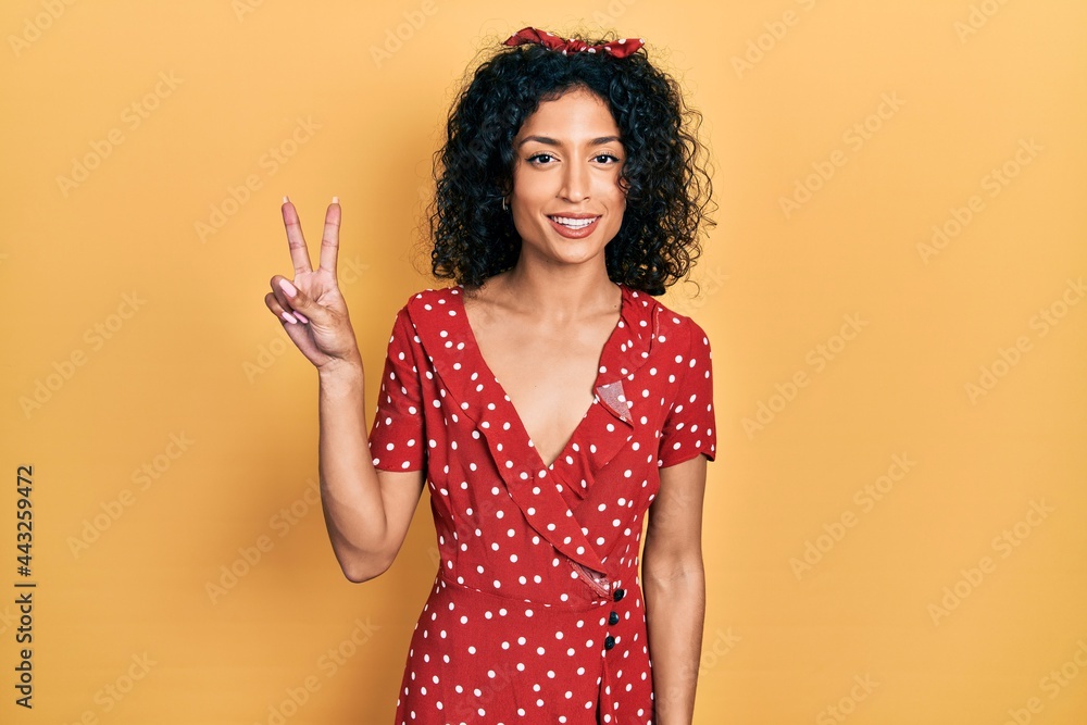 Young latin girl wearing summer dress smiling looking to the camera showing fingers doing victory sign. number two. Young latin girl wearing summer dress smiling looking to the camera showing fingers doing victory sign. number two.