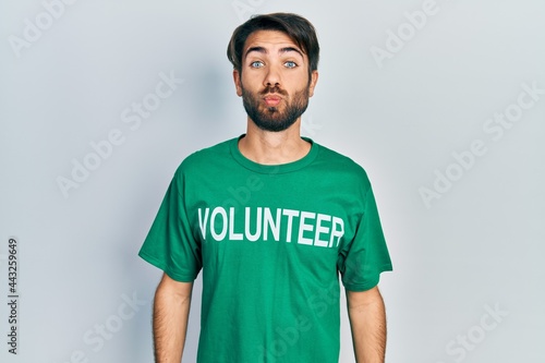 Young hispanic man wearing volunteer t shirt looking at the camera blowing a kiss on air being lovely and sexy. love expression.